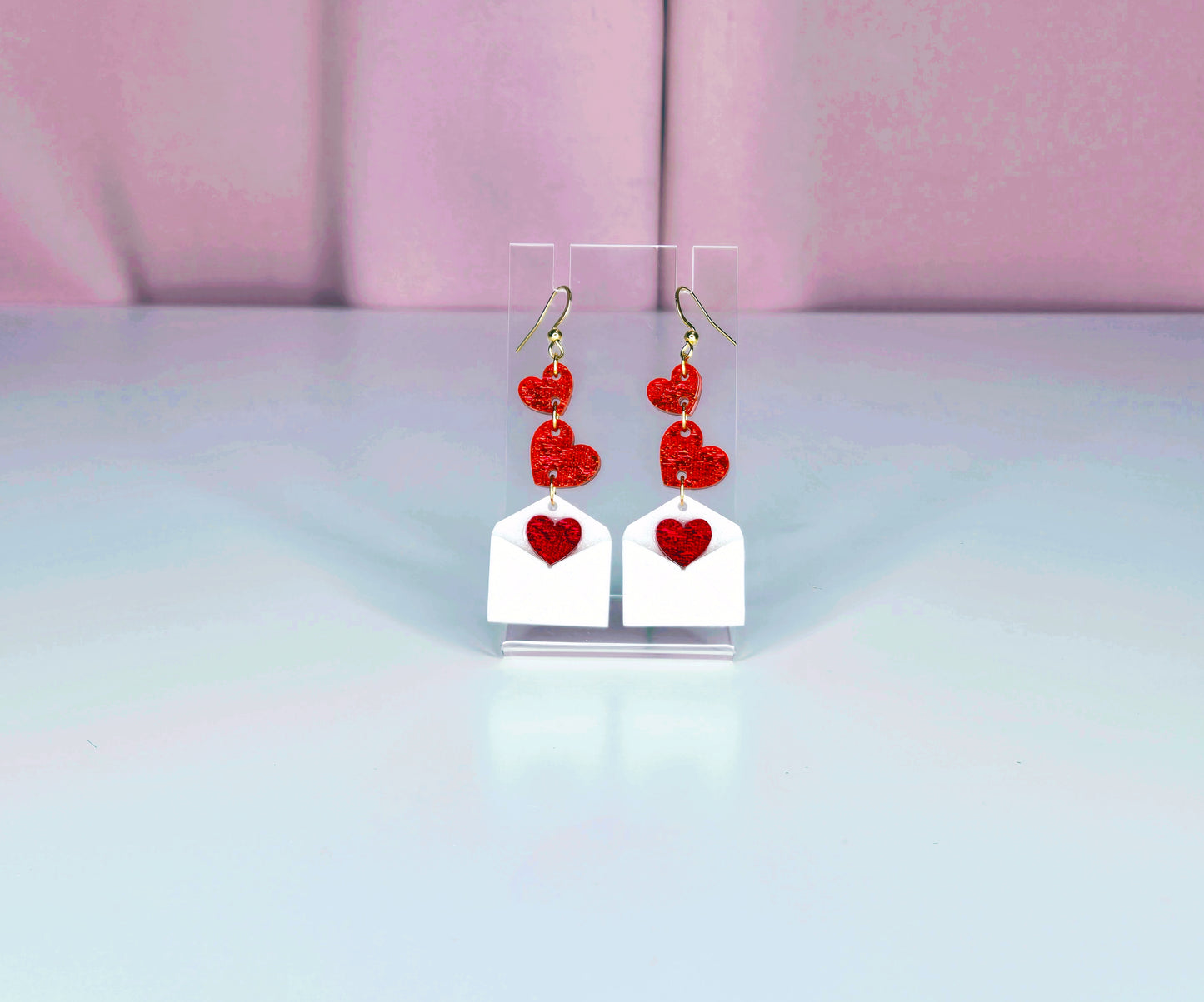 Earrings on a clear display against a white and pink background.