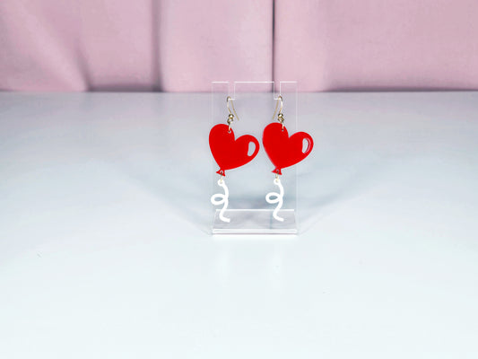 Earrings on a clear display against a white and pink background.