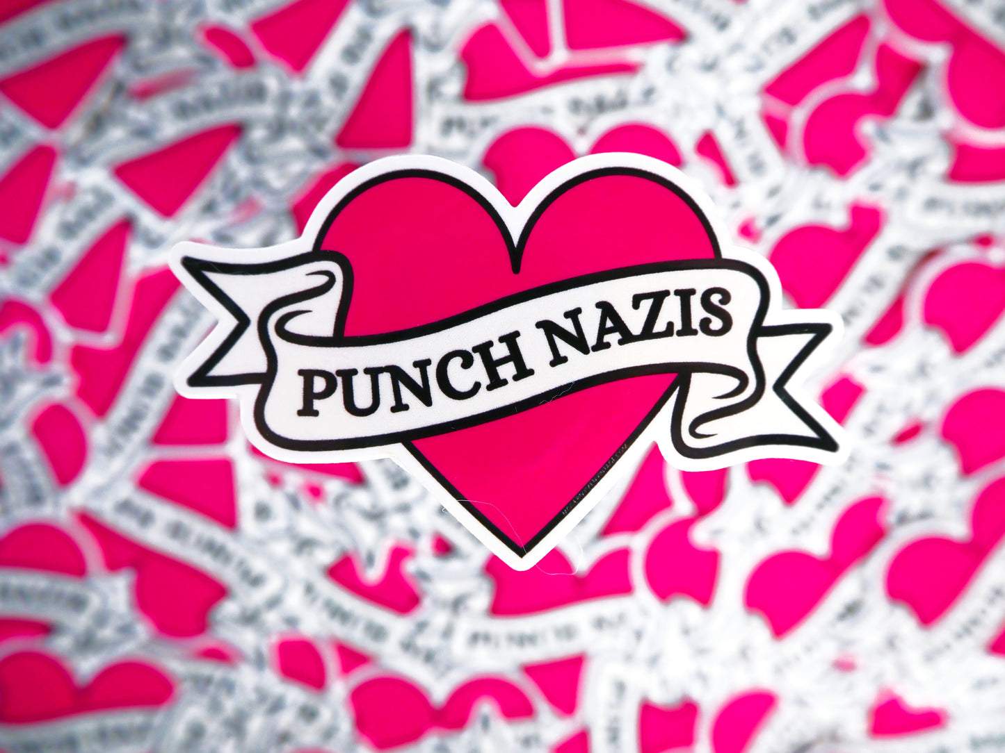 Heart-shaped sticker with 'Punch Nazis' text on a pink and gray patterned background.
