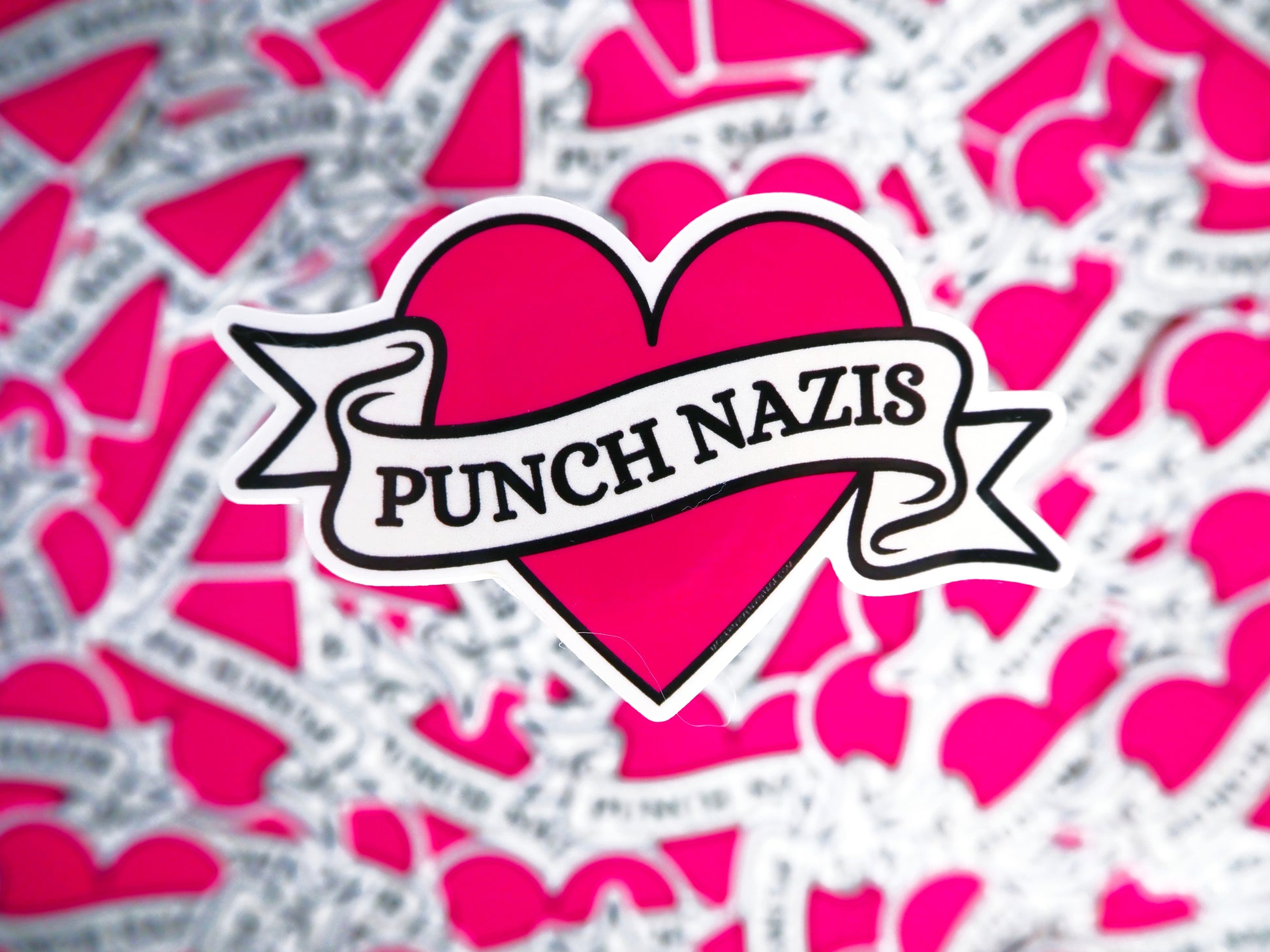 Heart-shaped sticker with 'Punch Nazis' text on a pink and gray patterned background.