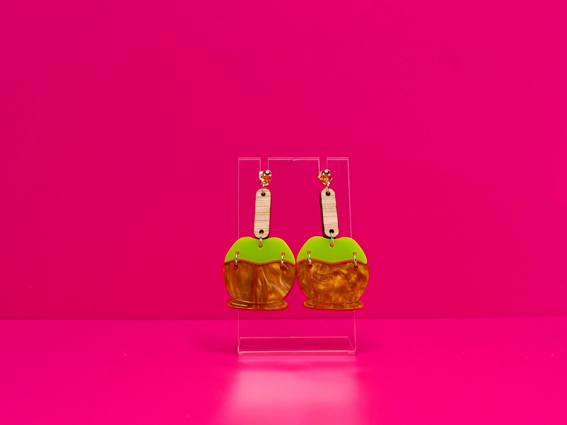 Earrings on a clear display against a hot pink background.