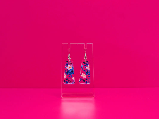 Blie and pink floral earrings on a clear stand against a pink background.