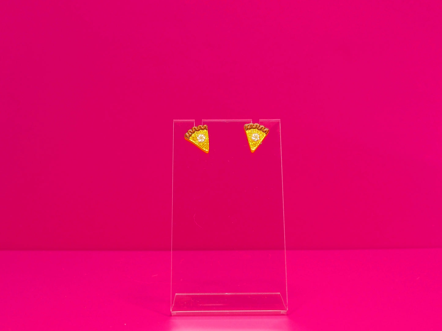 Earrings on a clear display against a hot pink background.