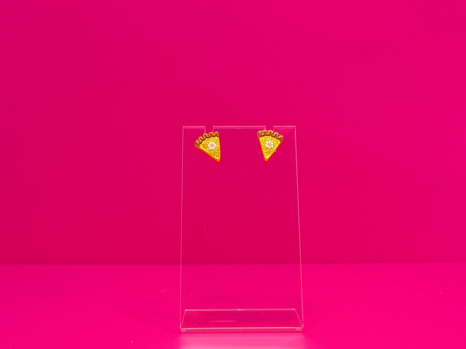 Earrings on a clear display against a hot pink background.