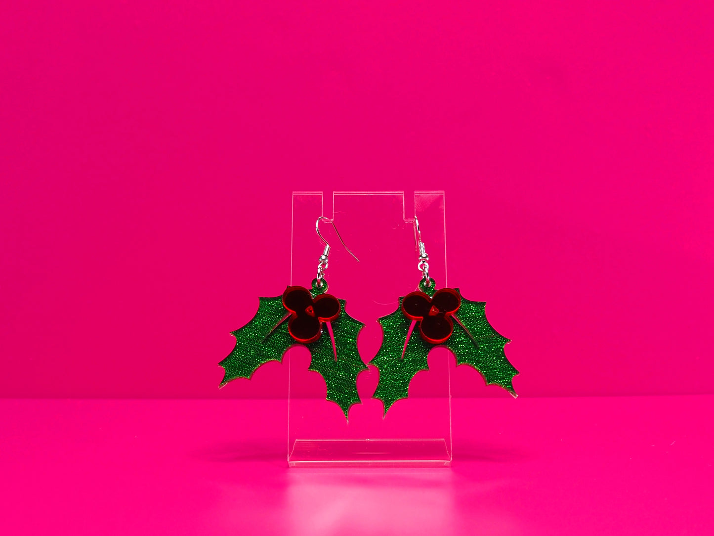 Holly leaf earrings against a hot pink background.