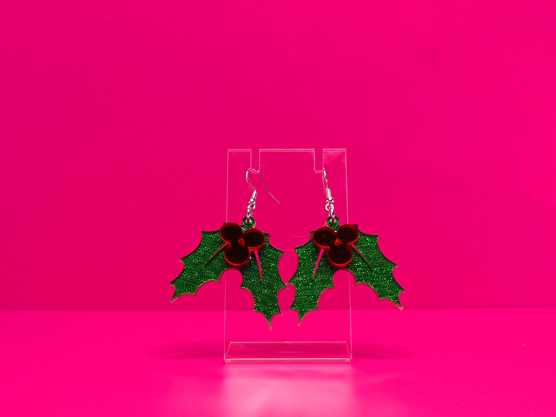 Holly leaf earrings against a hot pink background.