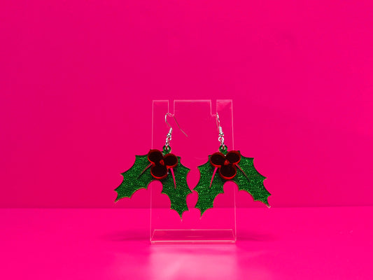Holly leaf earrings against a hot pink background.