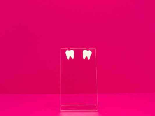 Pair of white tooth earrings on a clear display against a hot pink background.