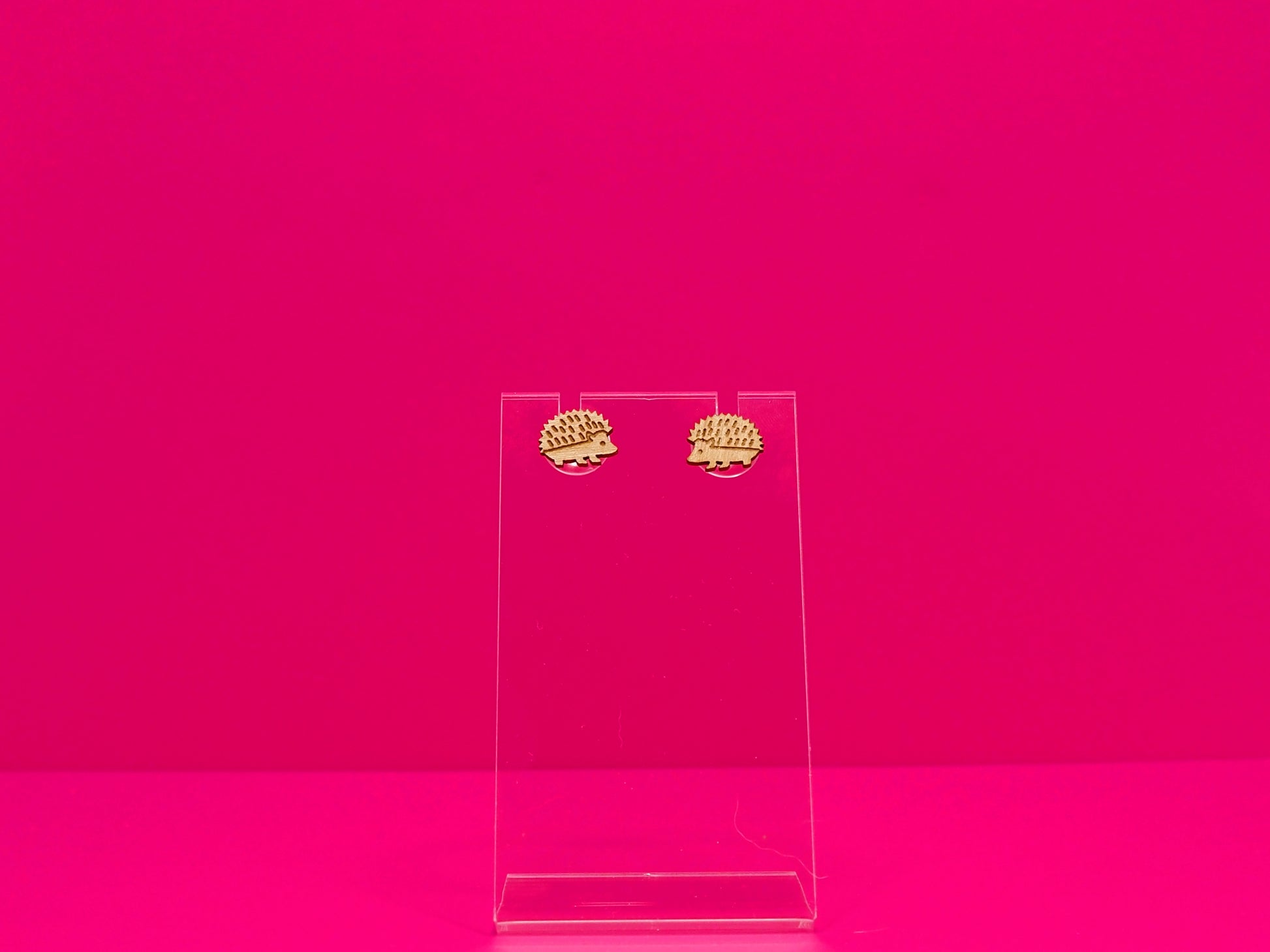 Light brown wood hedgehog earrings against a hot pink background.