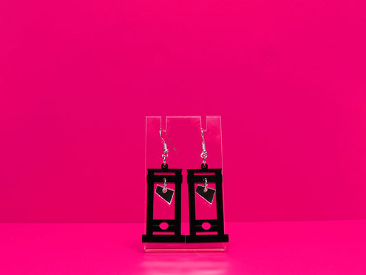 Black guillotine earrings on a clear display against a hot pink background.