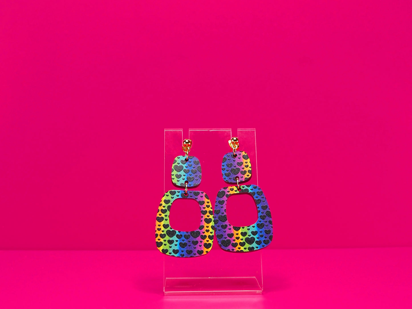 Rainbow earrings against a hot pink background.