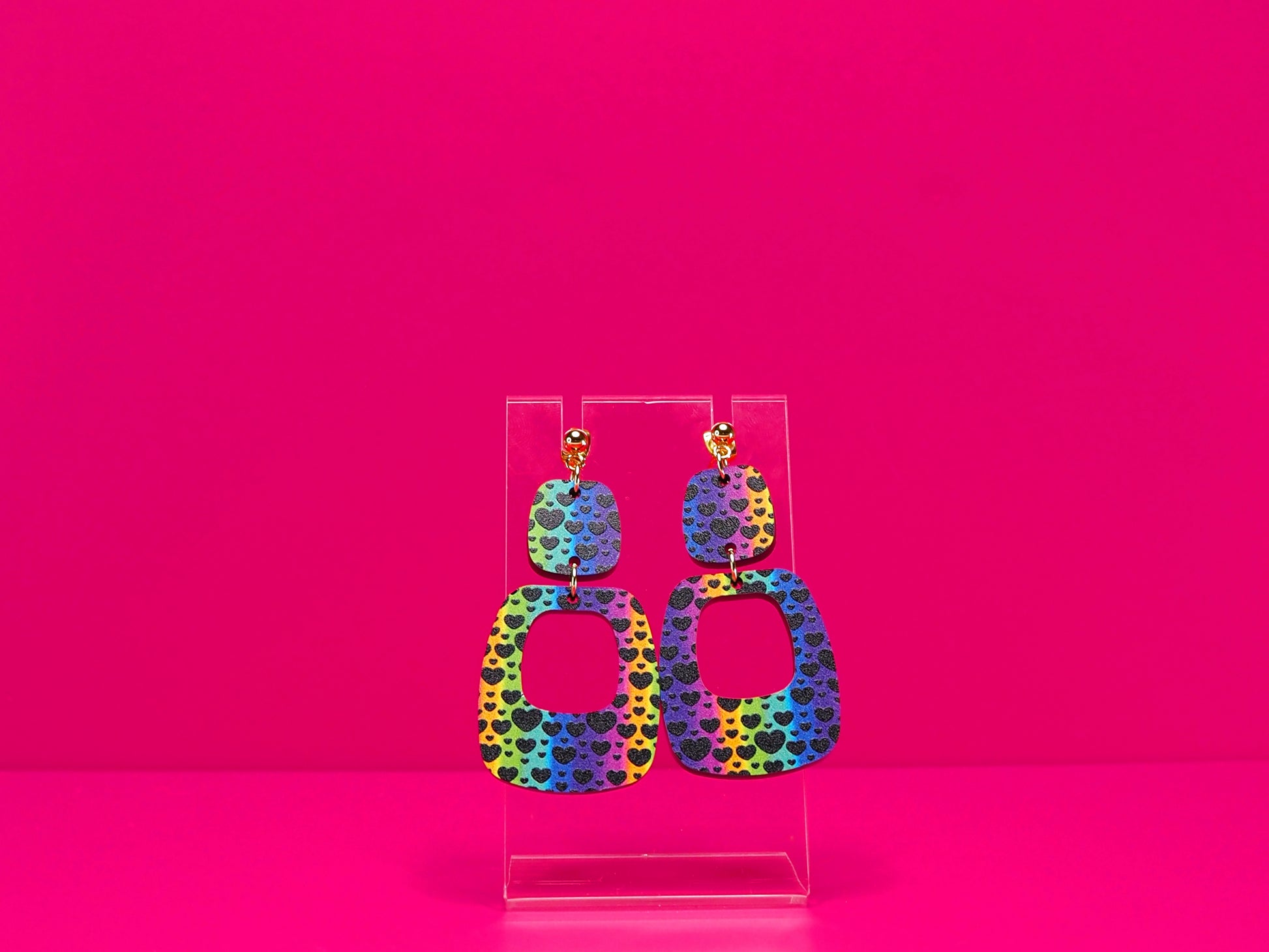 Rainbow earrings against a hot pink background.