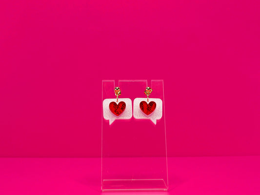 Red hearts on white text bubble earrings on a clear display against a pink background. Shown with gold studs option.