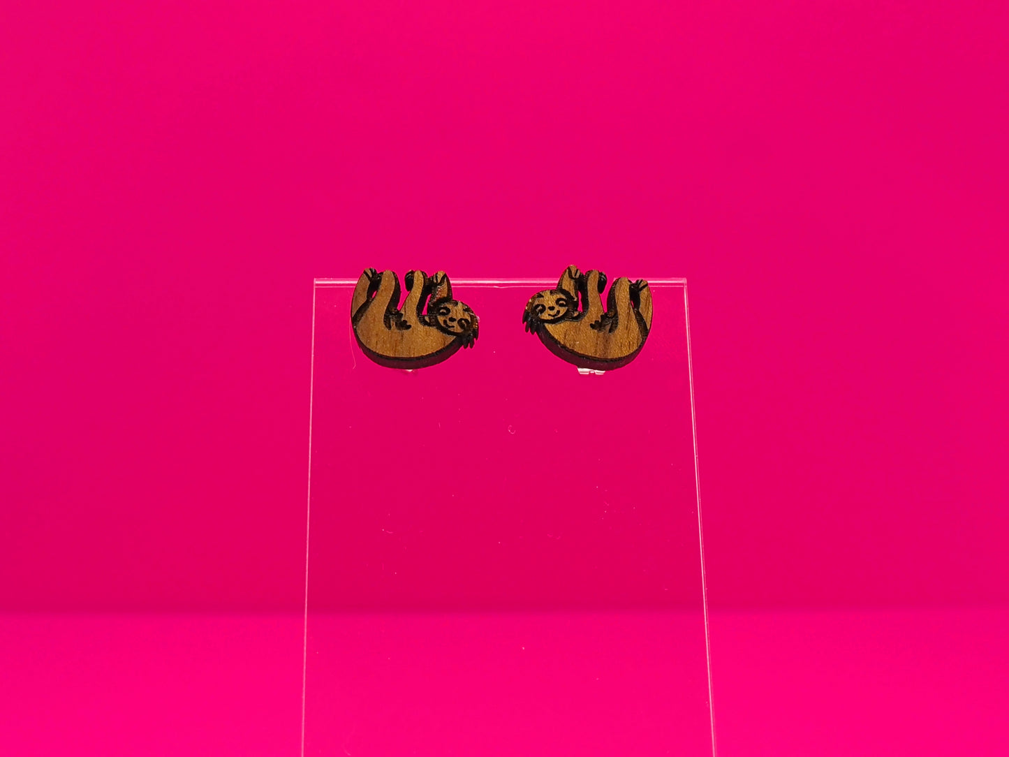 Pair of brown wood sloths on a clear display against a hot pink background.