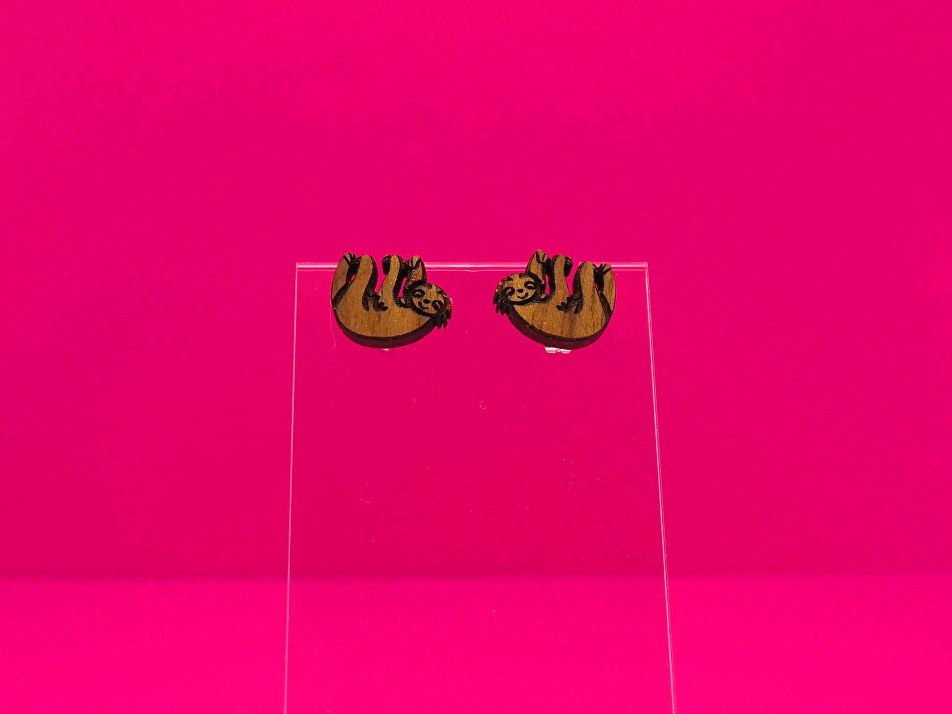 Pair of brown wood sloths on a clear display against a hot pink background.