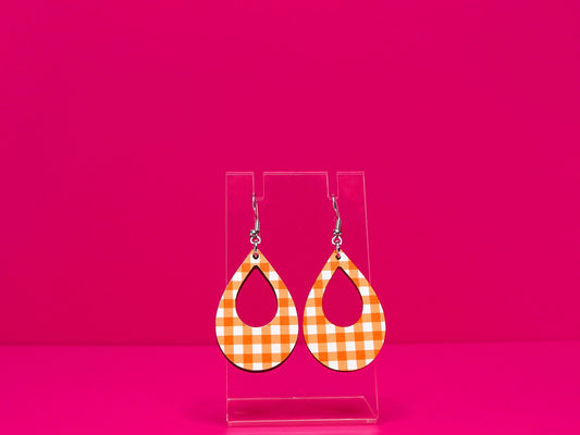 Orange gingham tear drop shaped earrings on a clear display against a hot pink background.