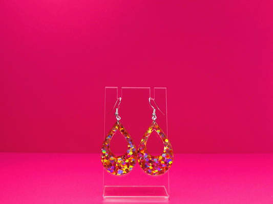 Pink glitter teardrop earrings on a clear display against a pink background.