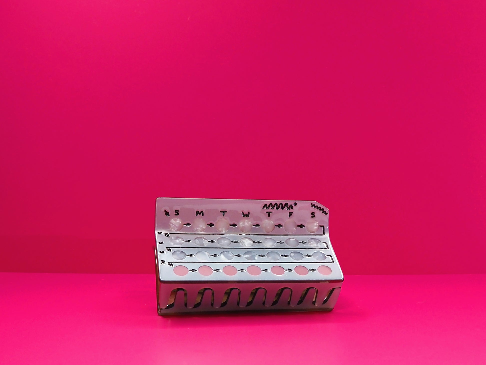 Birth control hair claw against a pink background.