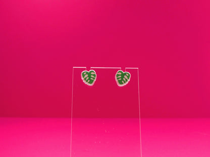 Monstera leaf earrings on a clear display against a pink background.
