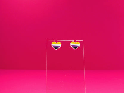 Non-binary pride heart earrings on a clear display against a pink background.