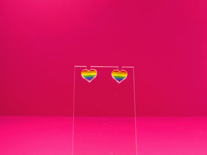 Rainbow pride heart earrings on a clear display against a pink background.
