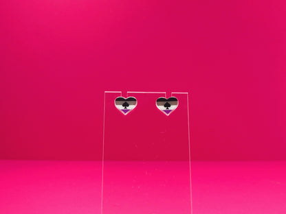 Ace pride heart earrings on a clear display against a pink background.