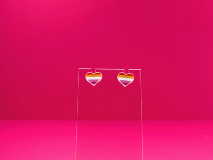 Lesbian pride heart earrings on a clear display against a pink background.