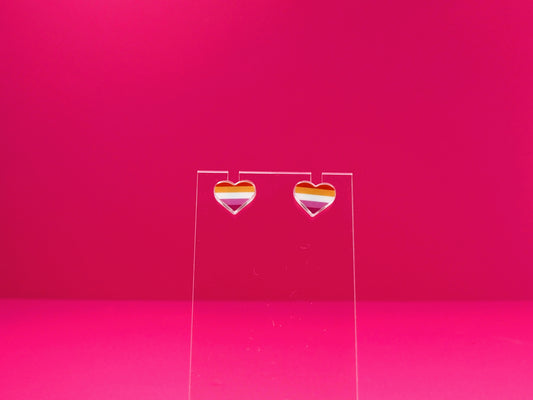 Lesbian pride heart earrings on a clear display against a pink background.