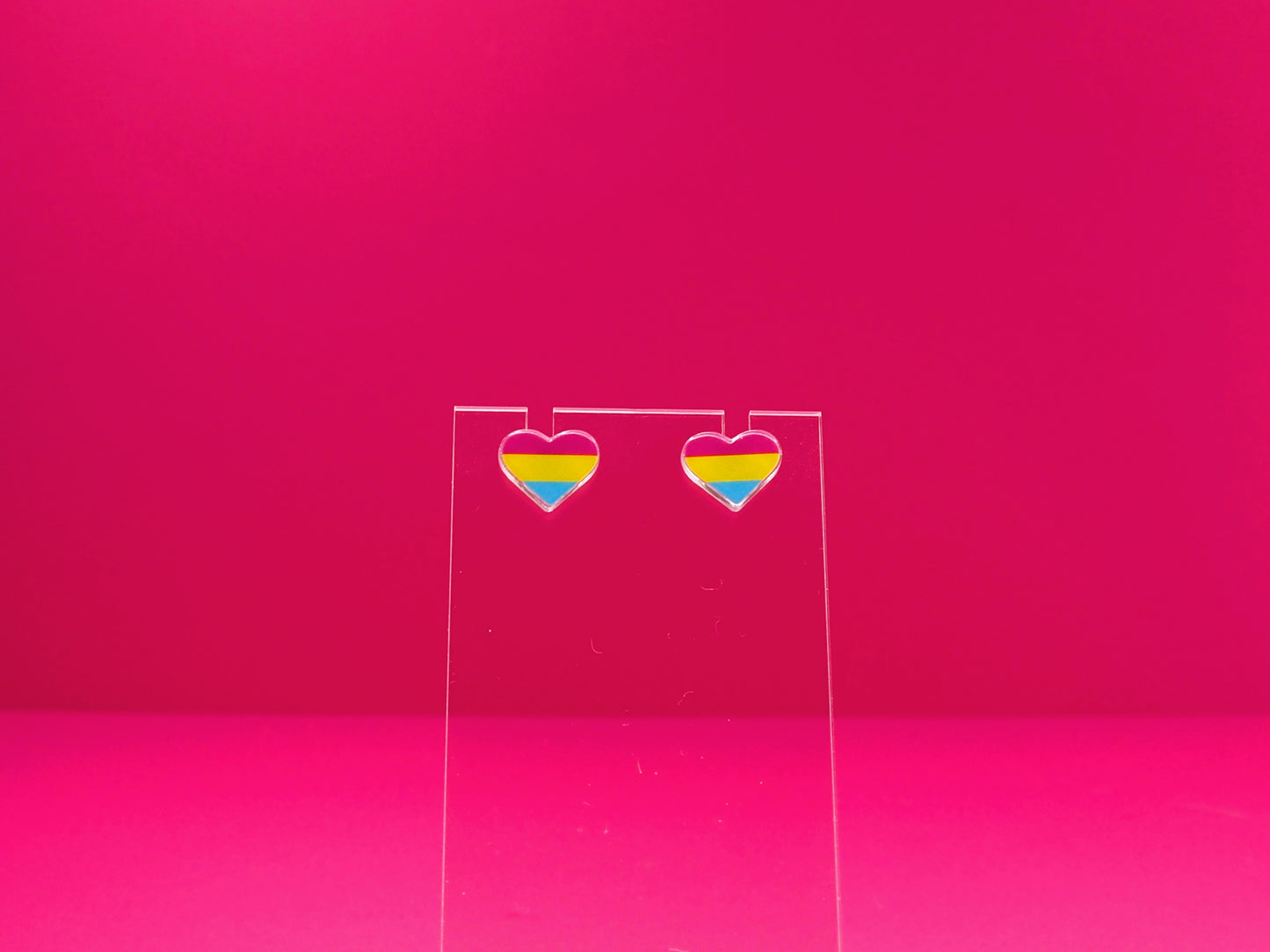 Pansexual pride heart earrings on a clear display against a pink background.
