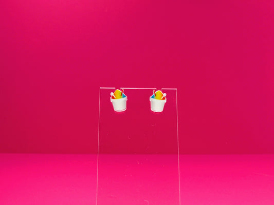Rainbow snoball earrings on a clear display against a pink background.