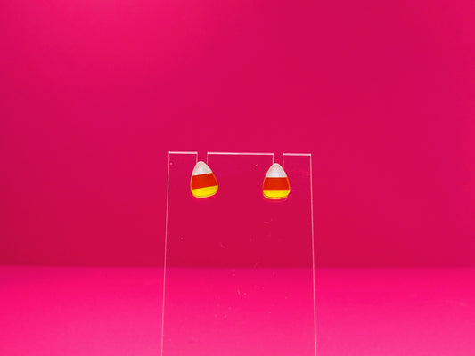 Candy corn earrings on a clear display against a pink background.