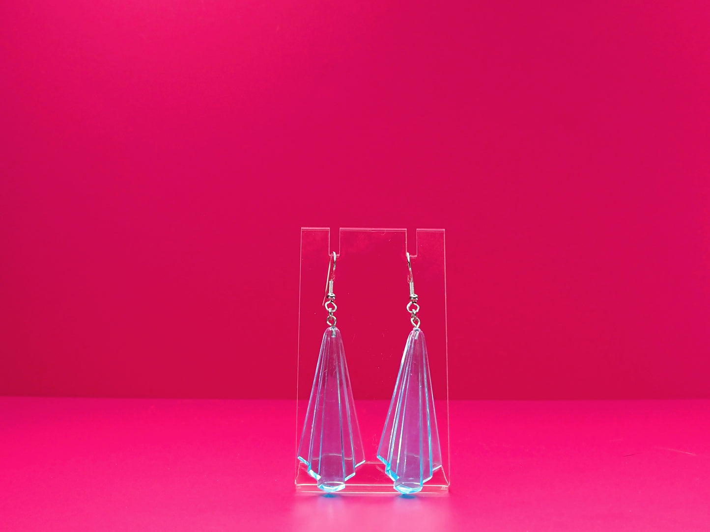 Art deco earrings on a clear display against a pink background.