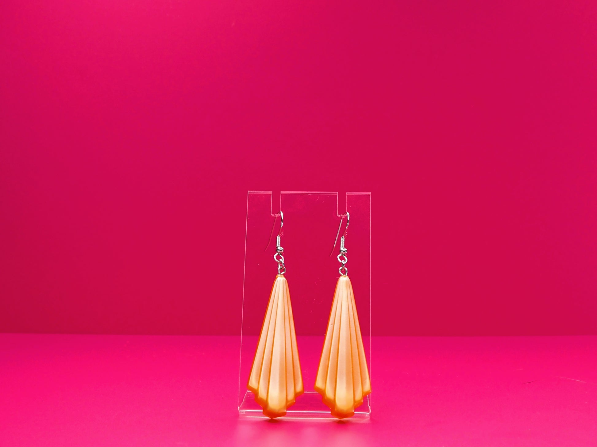 Art deco earrings on a clear display against a pink background.