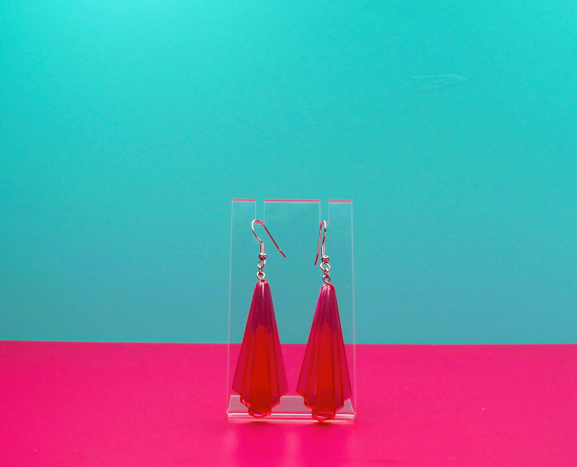 Pink art deco earrings against a blue and pink background.