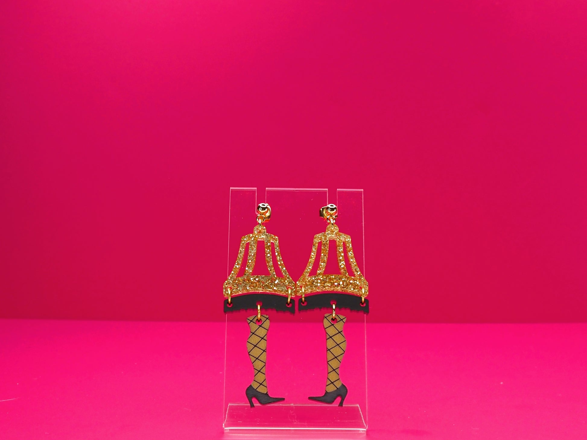 Leg lamp earring on a clear display against a pink background.