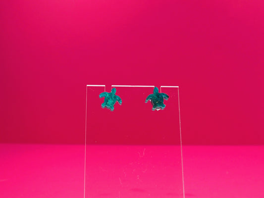 Marbled green sea turtle earrings on a clear display against a pink background.