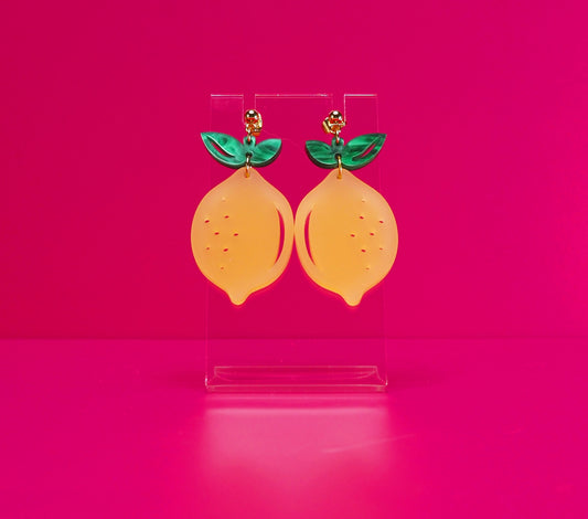 Lemon earrings on a clear stand against a pink background.