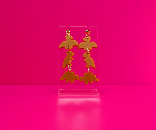 Dinosaur nugget earrings on a clear stand against a pink background.