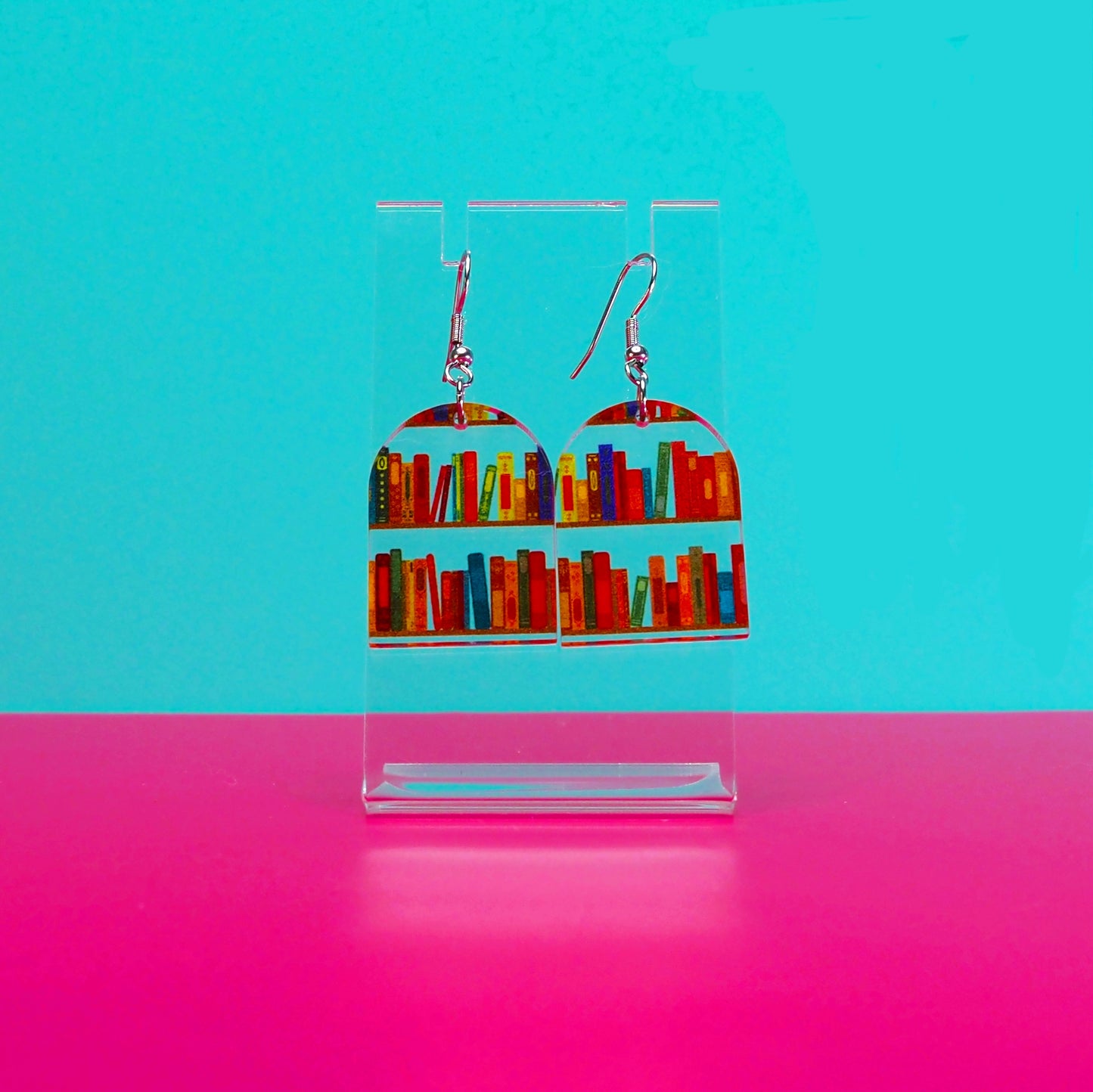 Earrings on a clear stand against a blue and pink background.