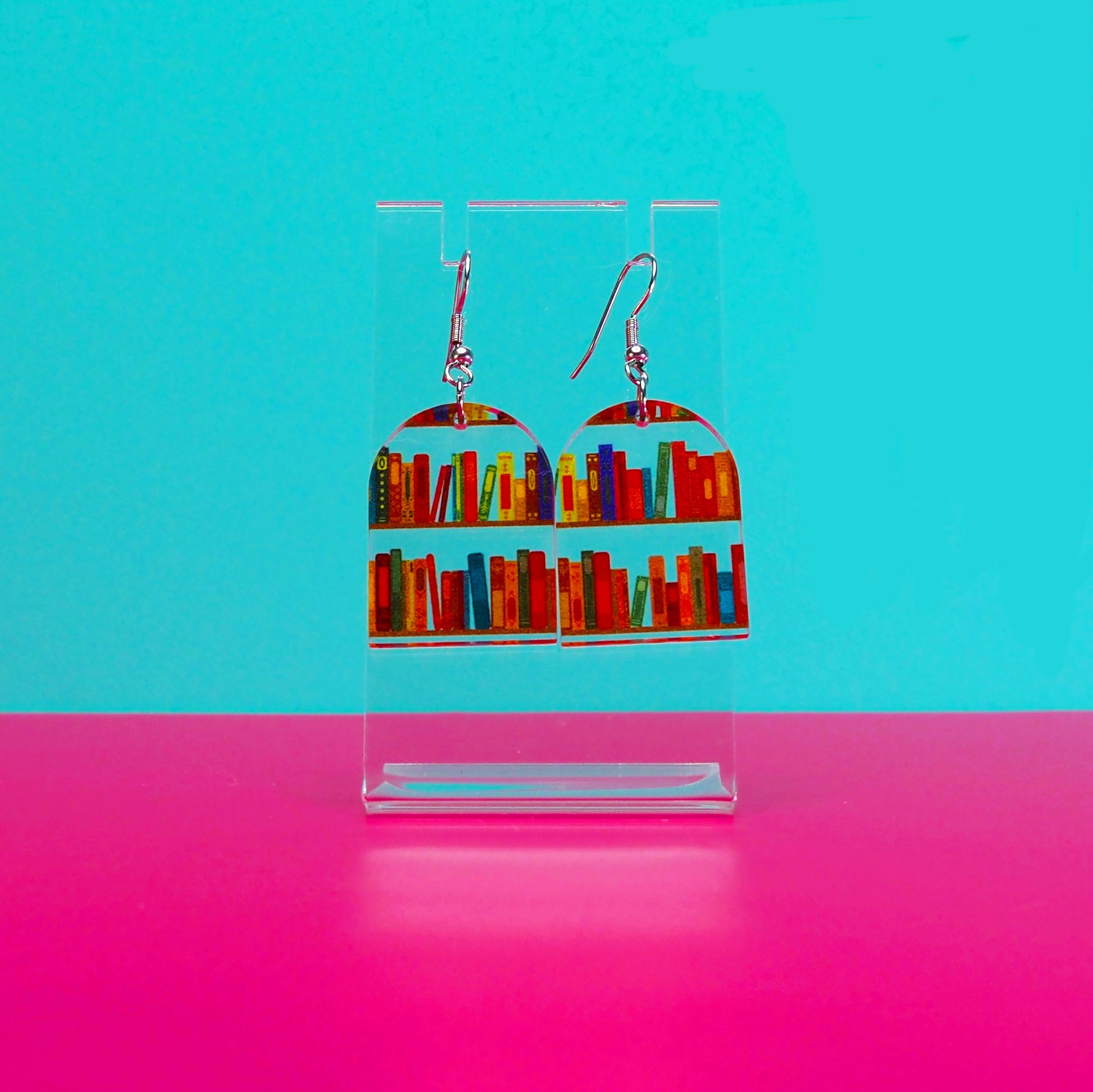 Earrings on a clear stand against a blue and pink background.