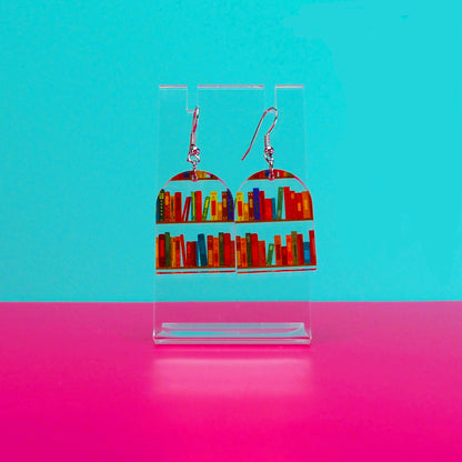 Earrings on a clear stand against a blue and pink background.