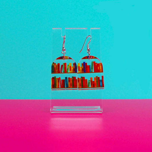 Earrings on a clear stand against a blue and pink background.