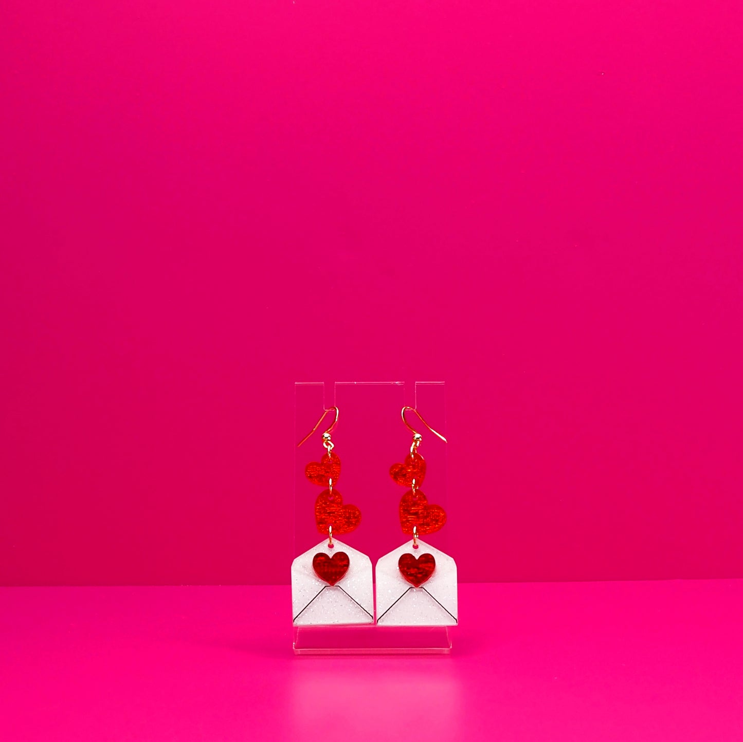 Red hearts cascading into a white envelope on a clear stand against a pink background.