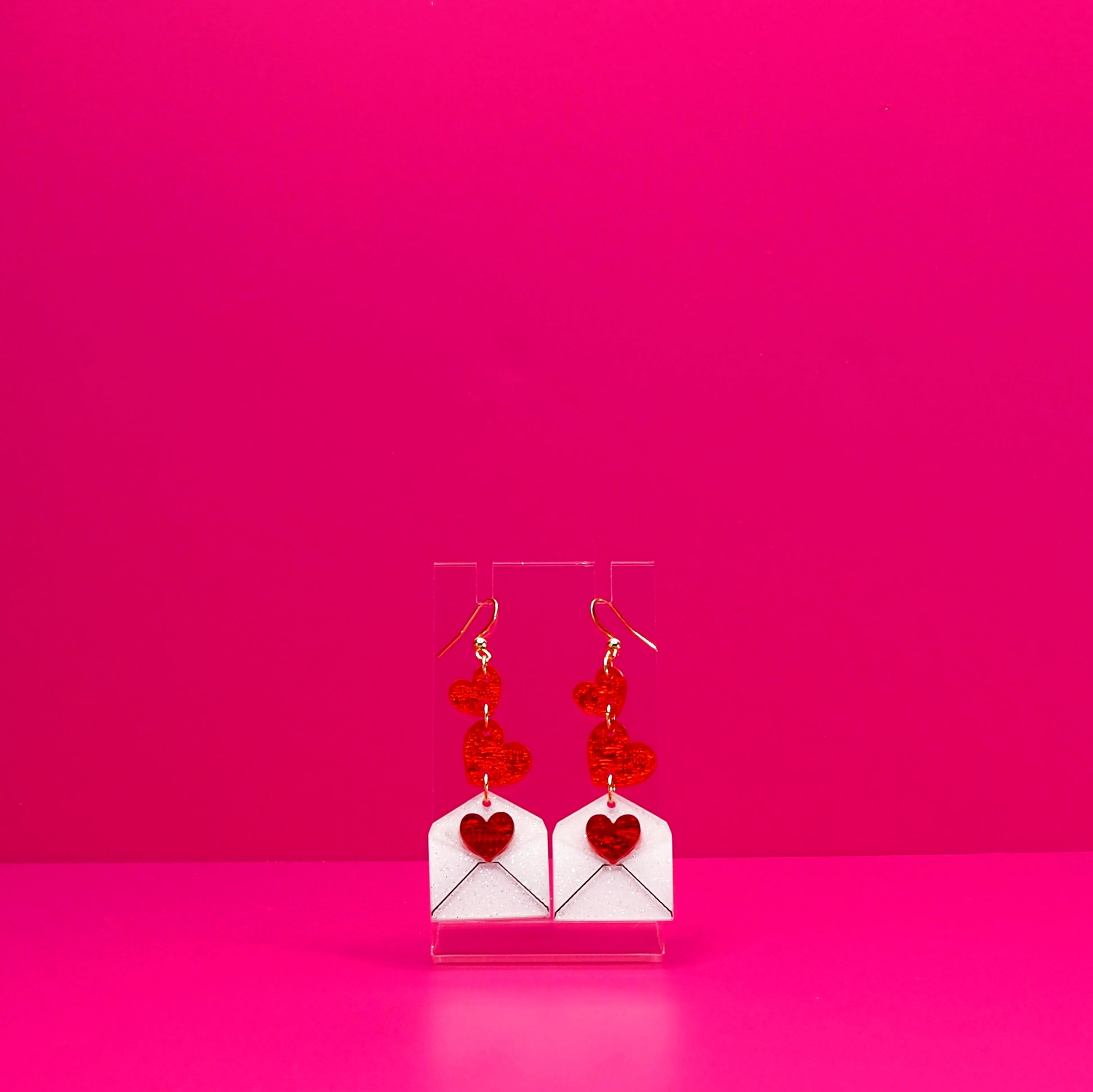 Red hearts cascading into a white envelope on a clear stand against a pink background.