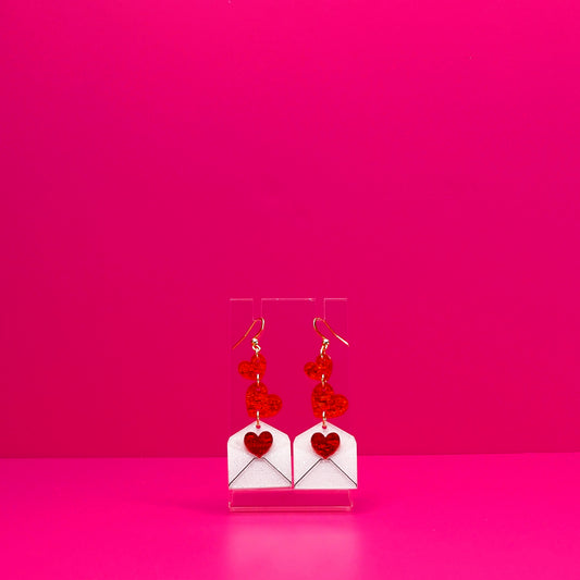 Red hearts cascading into a white envelope on a clear stand against a pink background.