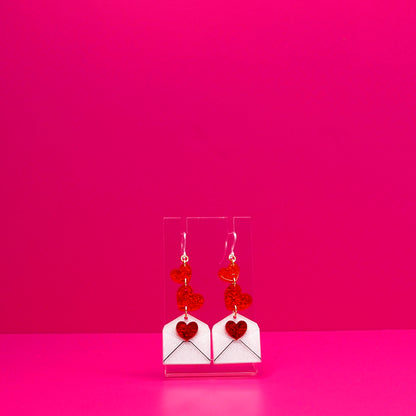 Red hearts cascading into a white envelope on a clear stand against a pink background.