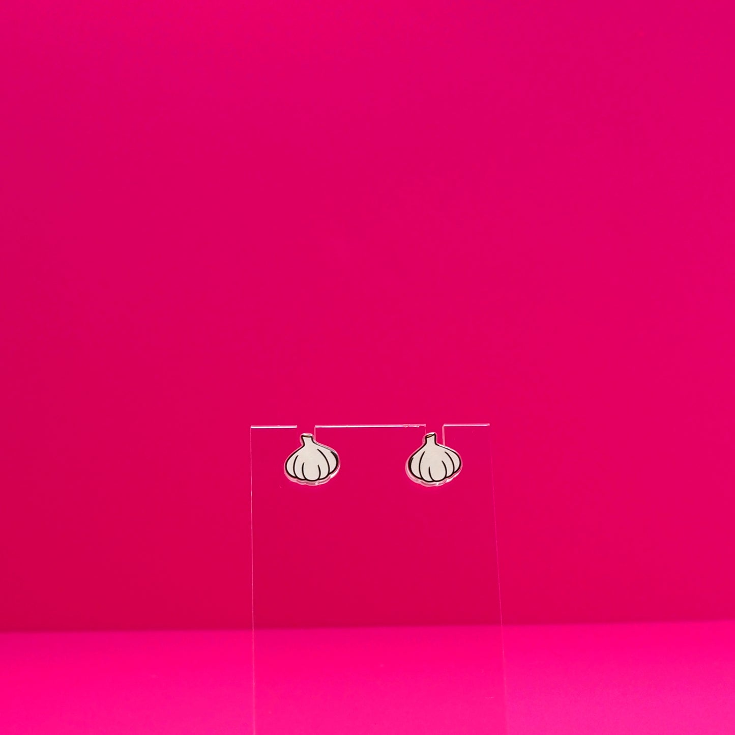 Garlic earrings on a clear stand against a pink background.