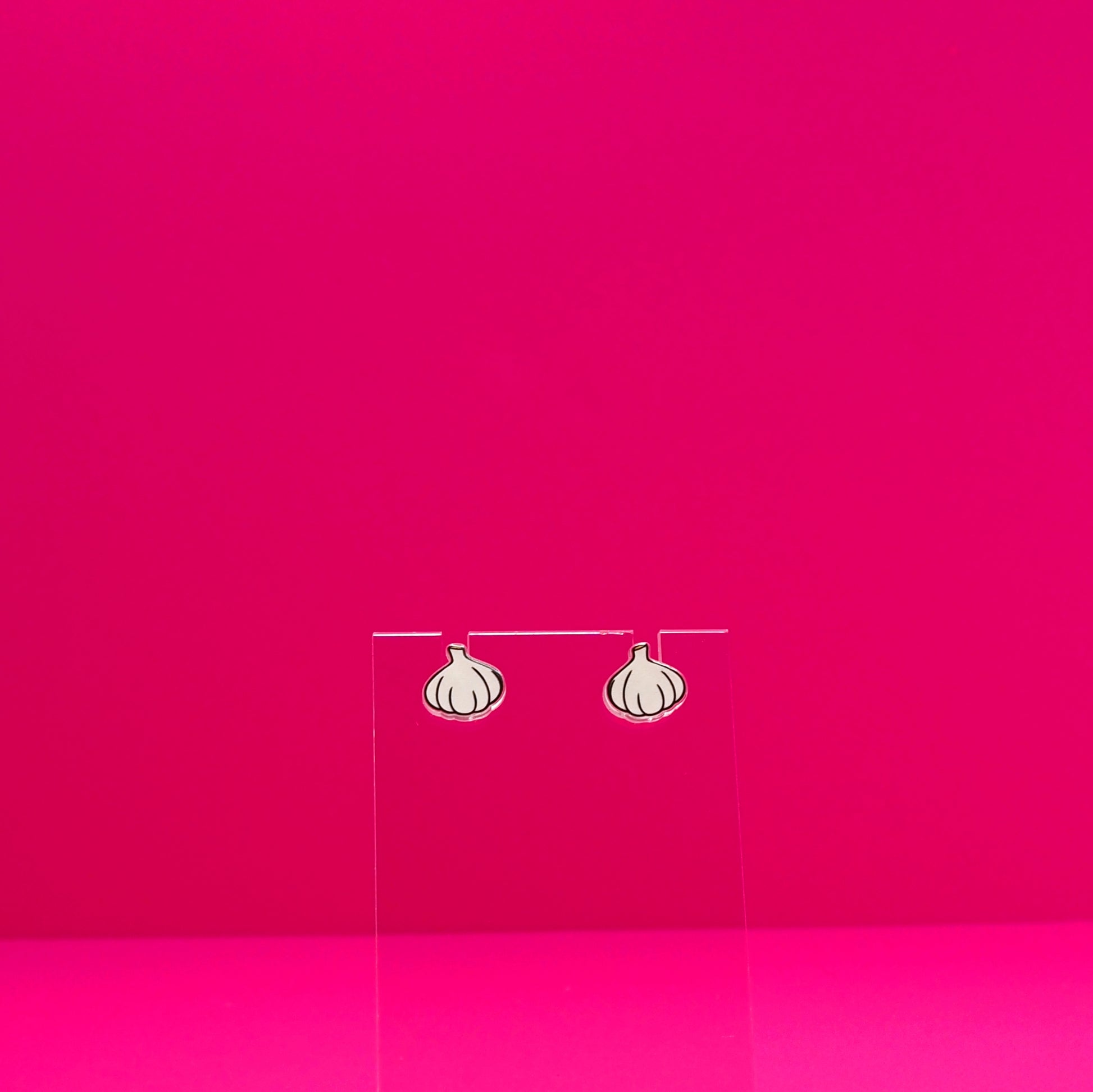 Garlic earrings on a clear stand against a pink background.