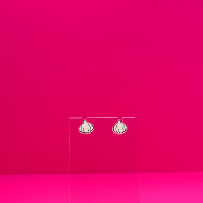 Garlic earrings on a clear stand against a pink background.
