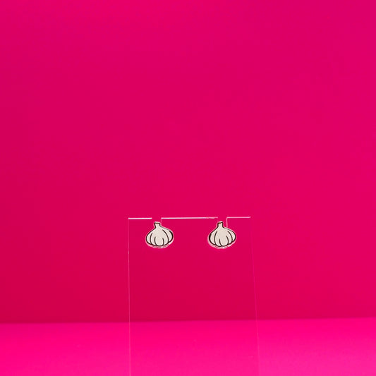 Garlic earrings on a clear stand against a pink background.